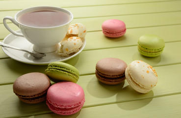 Tasty varicolored macaroons and cup of tea on a green wooden table.