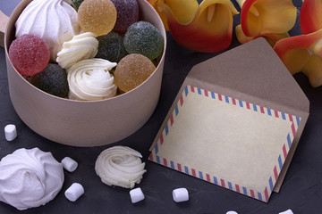 bouquet of red yellow callas with marshmallows marmalade in a wooden round box and envelope on gray concrete background.