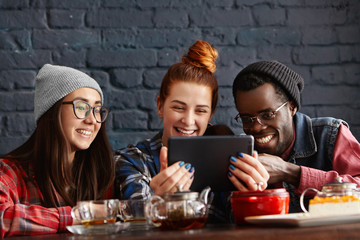 International group of fashionable African male, Caucasian and Asian girls making video call to their common friend, looking at screen with happy cheerful smiles, enjoying high-speed internet