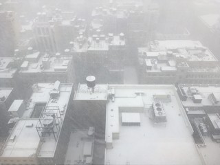 Looking out of a skyscraper window down on the snow-covered roofs below, Water tanks, air conditioning units, and rooftops covered in snow in Midtown Manhattan, NY.