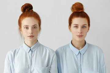 Indoor shot of two gorgeous redhead girls looking alike wearing same hair buns and identical shirts...