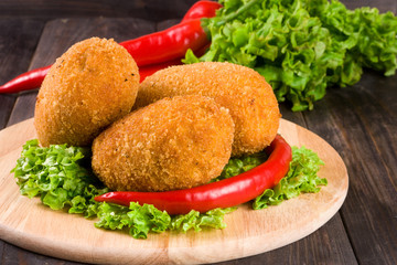 three fried breaded cutlet with lettuce on a cutting board and  wooden background