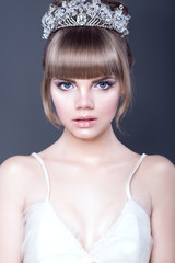 Fototapeta premium Portrait of young beautiful teenager girl with expressive blue eyes and full parted lips wearing jewel crystal crown looking straight ahead. Isolated on grey background. Close up. Studio shot