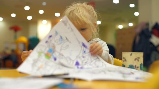 Adorable little blonde girl turns the page of the coloring book slow motion