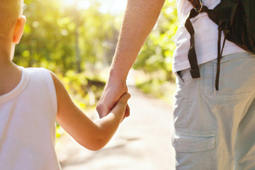 child holding hand of adult parent outside in summer park