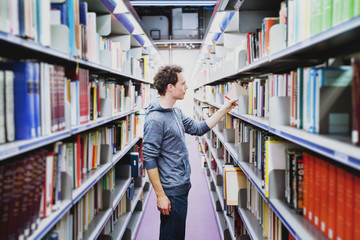 student in the library of university, young caucasian man taking book from bookshelf, education...
