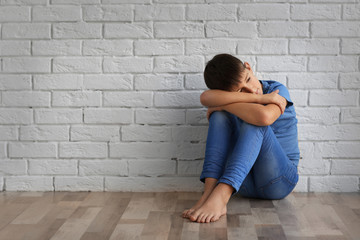Sad little boy sitting on floor against brick wall background
