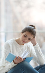 Obraz premium Young woman reading book on windowsill at home