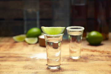 Tequila shot with juicy lime slice and salt on wooden table