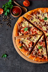 Home pizza with salami, tomato and cheese on a black background