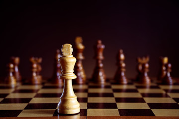 White chess king in front of a chessboard, black chess pieces on a dark background