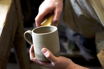 handmade clay pots, man adjusts fired clay cup, detail on man hands working in pottery 