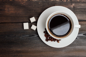 cup with a dark drink, coffee beans in a saucer and cubes of sugar