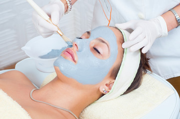 Woman lying on massage table in health spa while facial mask is applied on her face