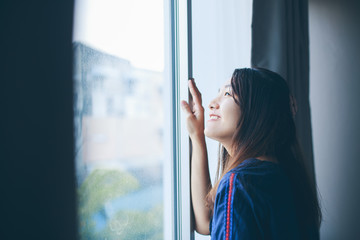 Pretty Asian woman standing by the window in the morning.