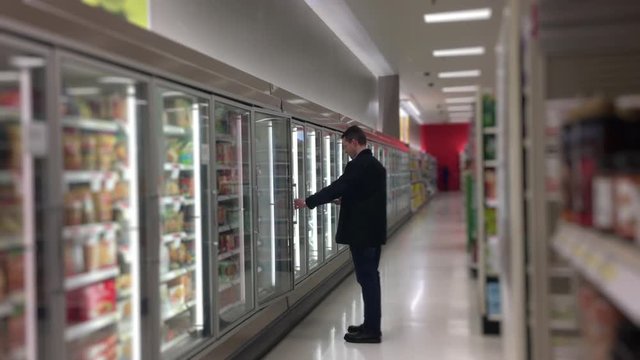 A man in a grocery store shops in the frozen foods section.	