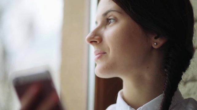 Beautiful young casual female using mobile phone and look at the window in her office.