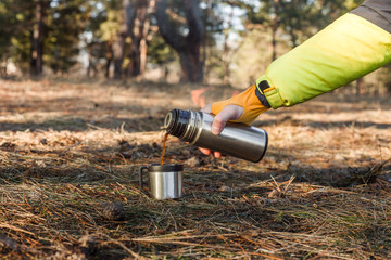 A thermos and a cup with hot coffee in the forest  background.