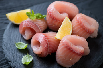 Close-up of marinated tilapia fillet rolls on a stone slate, selective focus