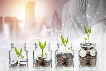 Fototapeta na wymiar Double exposure of success businessman using digital tablet with coins with seed in clear bottle,Business investment growth concept,saving concept on city landscape background