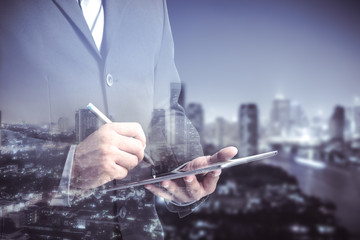 Double exposure of success businessman using digital tablet with city landscape background