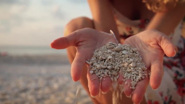 Close up woman's hands drizzling sea sand through her fingers against an ocean backdrop, conceptual image