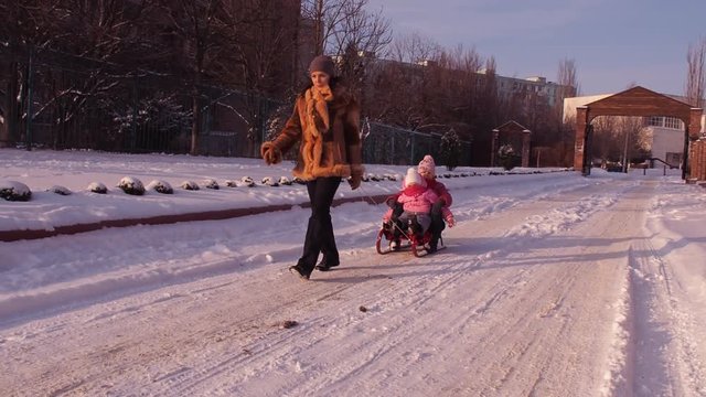 Mom rolls children on a sled.