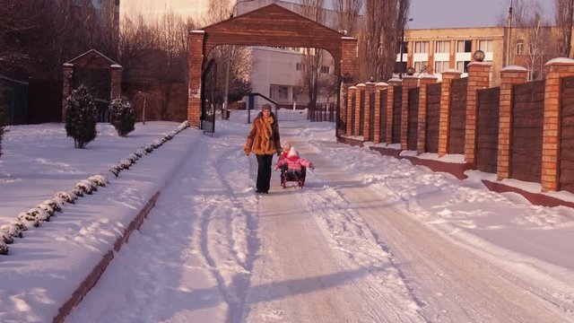 Mom rolls children on a sled.