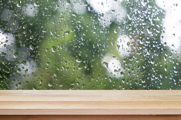 Brown wood table floor scene of water rain drop on window glass with relax green leaf view....