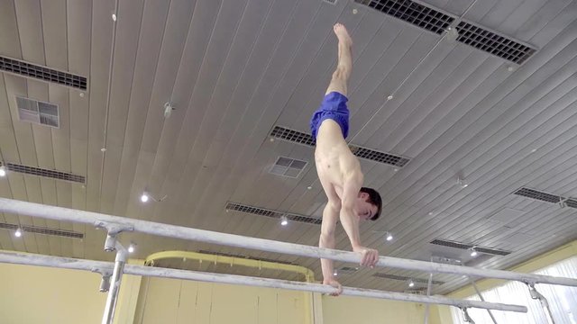 Gymnast performs routine on parallel bars HD gymnastics slow-motion video. Olympics athlete training skills and doing swings acrobatic exercises: hand support, somersault, flip