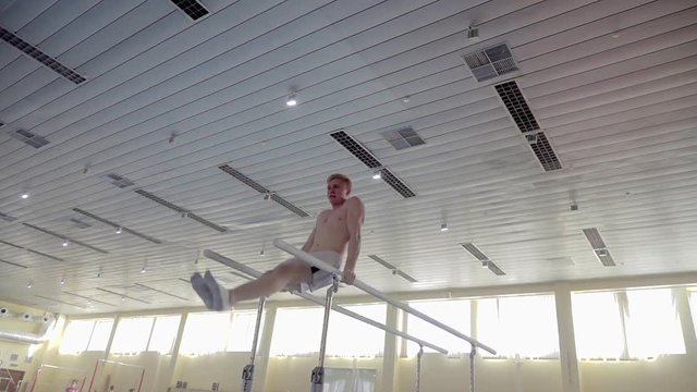 Gymnast performs routine on parallel bars HD gymnastics slow-motion video. Olympics athlete training skills and doing swings acrobatic exercises: hand support, somersault, flip