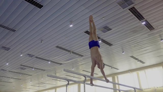 Gymnast performs routine on parallel bars HD gymnastics slow-motion video. Olympics athlete training skills and doing swings acrobatic exercises: hand support, flip, handstand