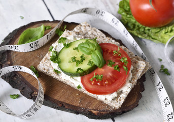 Healthy eating or dieting scene with crisp bread and fresh tomatoes and cucumber.
Tape measure and wooden table.