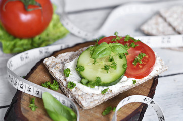 Healthy eating or dieting scene with crisp bread and fresh tomatoes and cucumber.
Tape measure and wooden table.