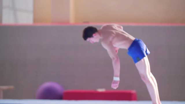 Young gymnast doing tumbling gymnastics exercises: somersault HD slow-motion video. Olympics athlete training acrobatic skills: flip, heli, salto