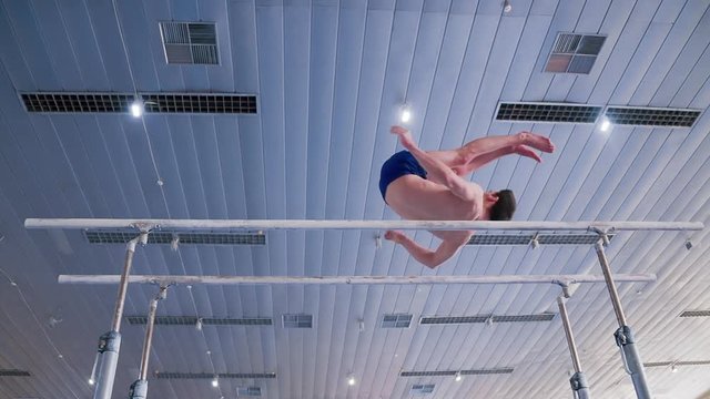Gymnast performs routine on parallel bars HD gymnastics slow-motion video. Olympics athlete training skills and doing swings acrobatic exercises: hand support, somersault, flip