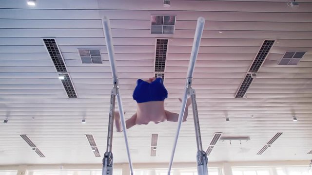 Gymnast performs routine on parallel bars HD gymnastics slow-motion video. Olympics athlete training skills and doing swings acrobatic exercises: hand support, somersault, flip