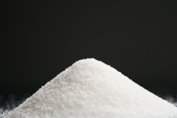 white sugar heap on black background closeup photo, shallow focus