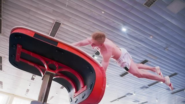 Gymnast performs gymnastic somersault exercises HD slow-motion video. Olympics athlete training acrobatic skills: jump and flip use sport equipment