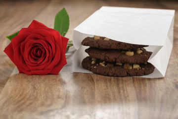 homemade chocolate cookies with chocolate chips and hazelnuts with red rose on wood table, shallow focus