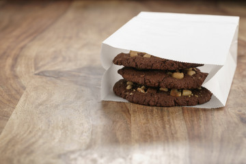 homemade chocolate cookies with chocolate chips and hazelnuts in paper bag on table, shallow focus