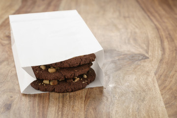 homemade chocolate cookies with chocolate chips and hazelnuts in paper bag on table, shallow focus