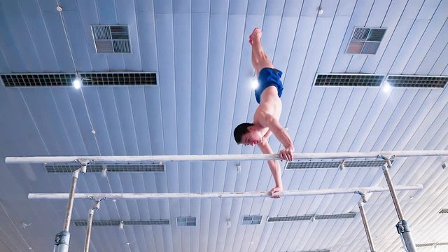 Gymnast performs routine on parallel bars HD gymnastics video. Olympics athlete training skills and doing swings acrobatic exercises: hand support