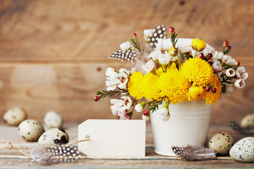 Easter greeting card with colorful flowers, feather and quail eggs on rustic wooden background. Beautiful spring composition.