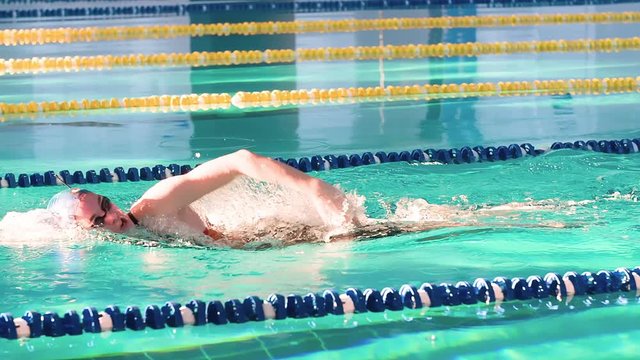 Female swimmer swims in pool HD slow-motion video. Front crawl freestyle training of professional woman athlete. Water splashing of arms stroke. Side view