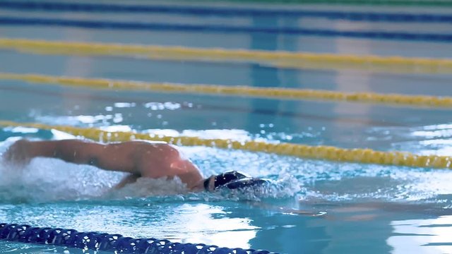 Male swimmer swims in pool HD slow-motion video. Front crawl freestyle training of professional man athlete. Water splashing of arms stroke. Side view