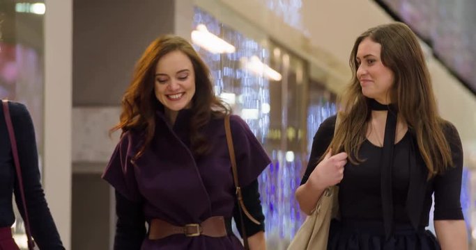 Female friends walk at shopping mall with sale bags HD video. Young women shoppers go past boutique with purchases, talk, smile and happy
