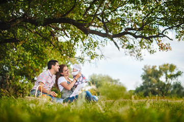 Naklejka na ściany i meble Happy family on a picnic. Mom and dad playing with a baby