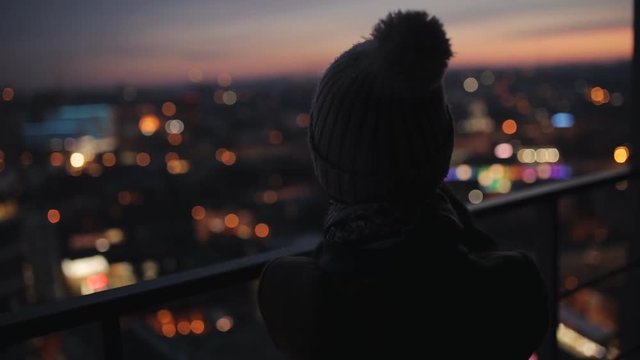 Woman photographing evening cityscape from high skyscraper. City night lights.
