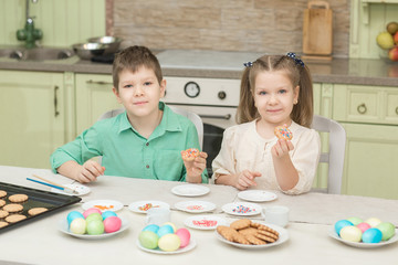 Fototapeta premium Cute children decorate cookies at a table in the home kitchen